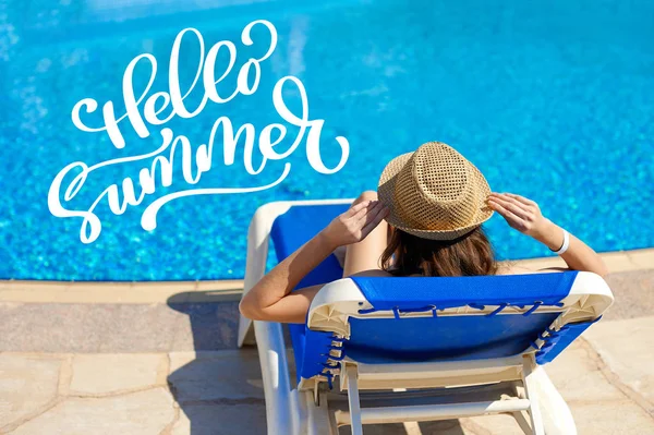 Женщина в соломенной шляпе расслабляется на шезлонге возле роскошного бассейна и букв Hello Summer, concept time to travel — стоковое фото