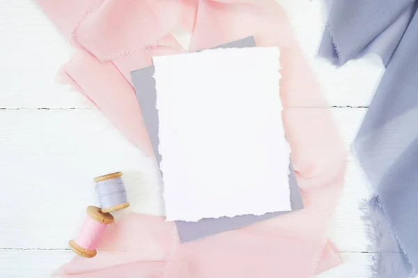 Witte lege kaart op een achtergrond van roze en blauwe stof op een witte achtergrond. Mockup met envelop en lege kaart. Flat lag. Bovenaanzicht — Stockfoto