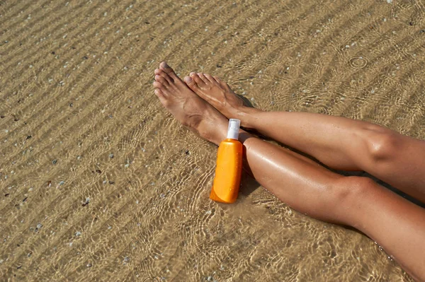 Schöne, gepflegte Frauenbeine mit einer Creme, um Sonnenbrand vor der Sonne im Sommer auf dem Hintergrundmeer zu schützen. Sorgt für saubere und weiche Haut. leerer Platz für einen Text — Stockfoto