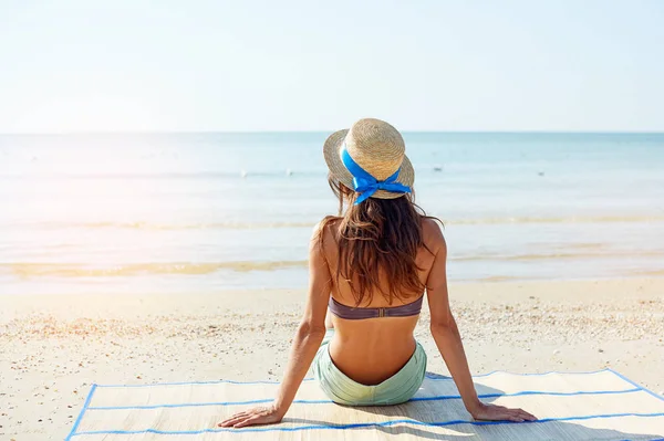 Sommer-Lifestyle-Porträt einer hübschen jungen, sonnengebräunten Frau mit Hut. Das Leben genießen und am Strand sitzen, Zeit zum Reisen. Blick auf das Meer — Stockfoto