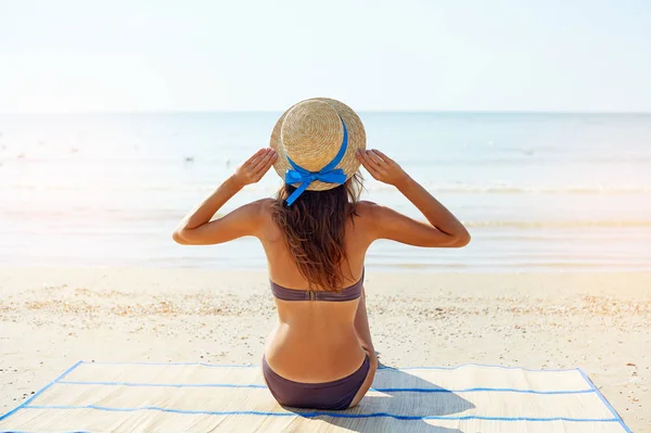 Retrato de estilo de vida de verano de una mujer bronceada joven y bonita con sombrero. Disfrutando de la vida y sentado en la playa, tiempo para viajar. Mirando al mar — Foto de Stock