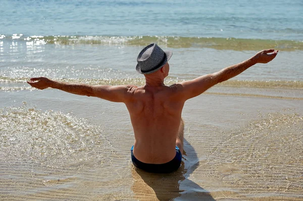 Portrait style de vie d'été d'un jeune homme bronzé dans un chapeau. Profitant de la vie et assis sur la plage, le temps de voyager. En regardant la mer — Photo