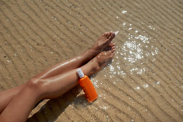 Piękne, zadbane womans nogi kremem do ochrony oparzenie słoneczne od słońca latem na tle morza. Dba o czystej i miękkiej skóry. Puste miejsce dla tekstu — Zdjęcie stockowe
