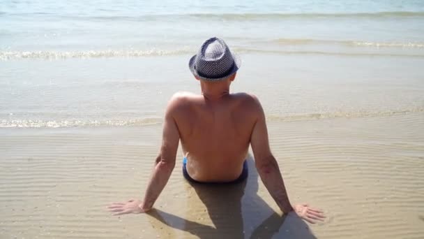 여름 모자에 꽤 젊은 구릿빛 남자의 라이프 스타일 Hd 비디오. 인생을 즐기는 하 고 해변에 앉아, 여행 시간. 바다를 보면 — 비디오