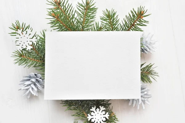 Feuille de papier blanche vide sur un fond de Noël blanc de branches et de cônes de sapin. Lettre sur Noël, maquette. Couché à plat sur un fond en bois blanc, avec place pour votre texte. Vue du dessus — Photo