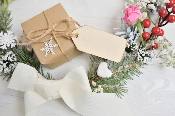 Fondo corona de Navidad con etiqueta de madera en blanco para su texto. Arco, regalo de Navidad, rosa rosa y conos. Composición festiva —  Fotos de Stock