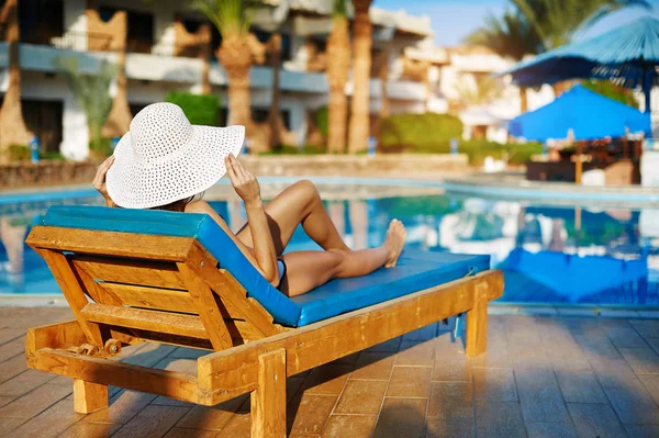 Frau mit weißem Hut liegt auf einer Liege in der Nähe des Swimmingpools im Hotel, Konzept Sommerzeit zu reisen — Stockfoto