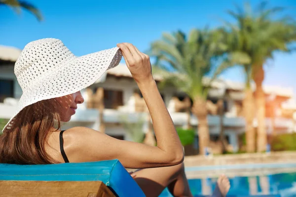 Vrouw in witte hoed liggend op een ligstoel bij het zwembad bij het hotel — Stockfoto