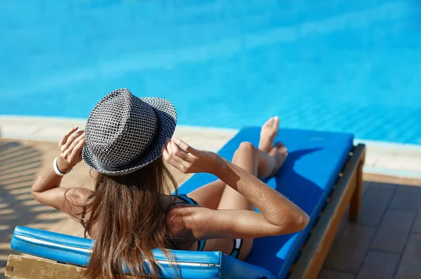 Frau mit Hut liegt auf einer Liege in der Nähe des Swimmingpools mit Platz für Ihren Text — Stockfoto