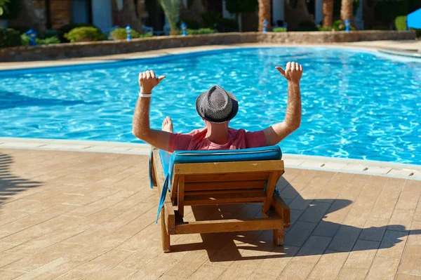 Jeune homme en chapeau et t-shirt rose se trouve sur plus fort et se détendre près de la piscine hôtel — Photo