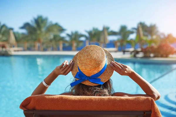 Jeune belle femme assise sur des chaises longues près de la piscine à l'hôtel en chapeau — Photo