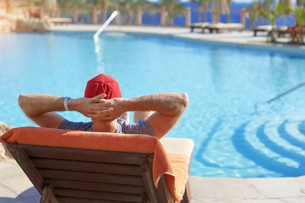 Hombre positivo en sombrero rojo descansando cerca del hotel piscina en Egipto. Concepto hermoso estilo de vida — Foto de Stock