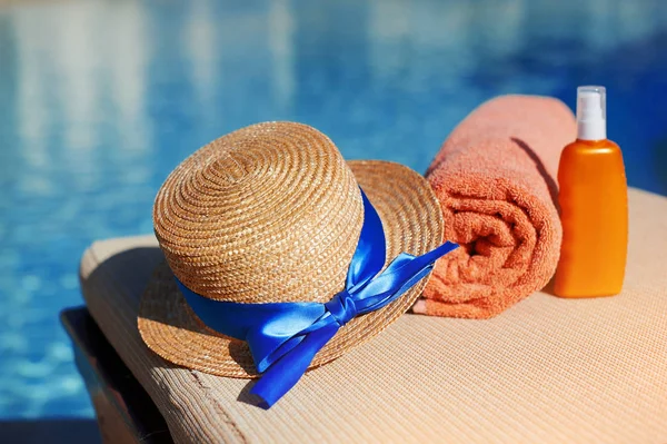Toalla de algodón naranja y crema solar para el cuerpo y sombrero en un tubo naranja en la piscina de fondo. Medios para el cuidado de la piel, el concepto de verano de relajación y protección solar — Foto de Stock