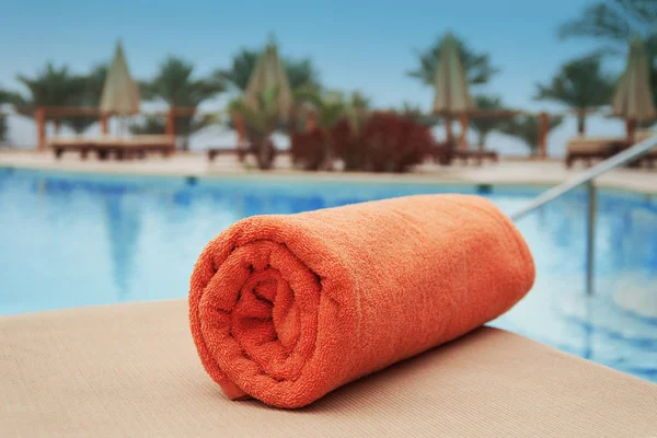 Toalla naranja tumbada en una tumbona cerca de la piscina del hotel verano — Foto de Stock