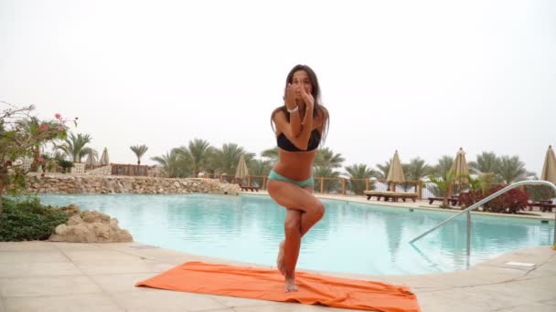 Vacker positiv kvinna sitter vid poolen på den orange handduken och mediterar i yogaställning — Stockvideo