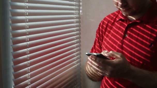 男子站在酒店房间的窗户附近, 使用智能手机 — 图库视频影像