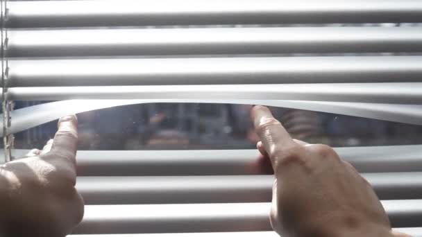 Doigts caucasiens ouvrant la fenêtre aveugle pour regarder dehors. En regardant à travers une fenêtre blanche aveugle pour voir dehors. Petits panneaux blancs — Video