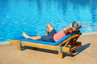Havuzu yaz aylarında rahatlamak. Genç ve başarılı adam şapkalı bir güneşlenme günbatımı, kavram zaman arka planda Hotel'in yatan seyahat etmek