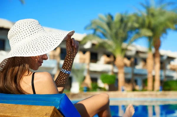 Frau mit großem weißen Hut liegt auf einer Liege in der Nähe des Swimmingpools im Hotel, Konzept Sommerzeit für Reisen in Ägypten — Stockfoto