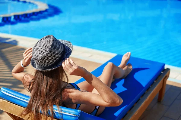 Mulher de chapéu deitada em uma espreguiçadeira perto da piscina do hotel, conceito hora de verão para viajar relaxar — Fotografia de Stock