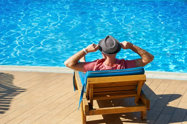 Détendez-vous dans la piscine en été. Jeune homme au chapeau couché sur une chaise longue à l'hôtel sur fond de coucher de soleil, concept time to travel — Photo