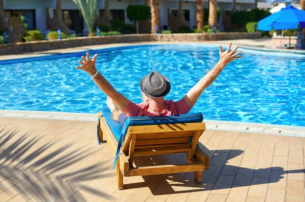 Relaxujte v létě bazén. Mladý a úspěšný muž v klobouku ležící na lehátku v hotelu na pozadí konceptu čas západu slunce, cestování — Stock fotografie