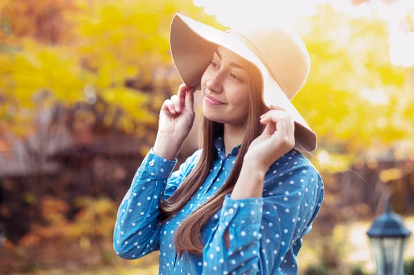 Beautiful young woman walking in autumn park. Gorgeous young woman in fall with big hat, smiling and enjoying nature — Stock Photo, Image