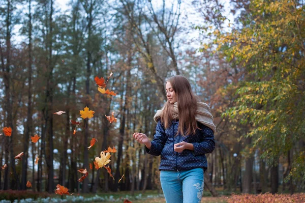 Outdoors lifestyle fashion image of happy beautiful girl throwing leaves up in the air in autumn park — Stock Photo, Image