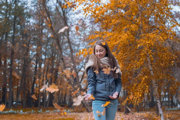 Модный образ жизнерадостной красивой девушки, бросающей листья в воздух в осеннем парке — стоковое фото