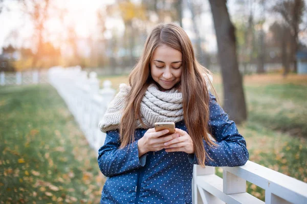 Sonbahar şehir parkında yürüyüş sırasında akıllı telefon kullanan mutlu genç kadın. — Stok fotoğraf