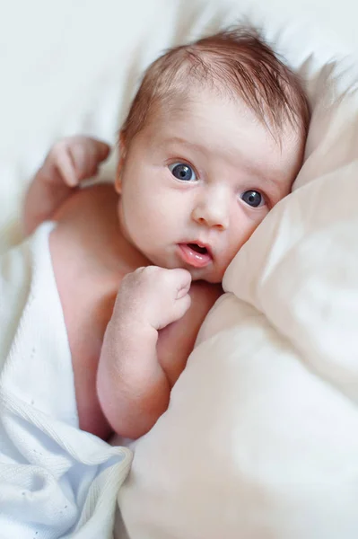 Retrato de un bebé recién nacido mirando a la cámara en una cama blanca —  Fotos de Stock