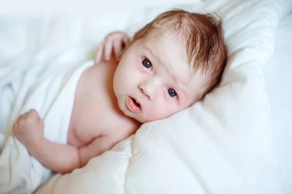 Retrato de un bebé recién nacido mirando a la cámara en una cama blanca —  Fotos de Stock