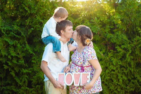 Gelukkige familie in het Park 's avonds licht. licht van de zon. Mam kussen van papa en vader te houden baby jongen. Het concept van een gelukkige familie — Stockfoto