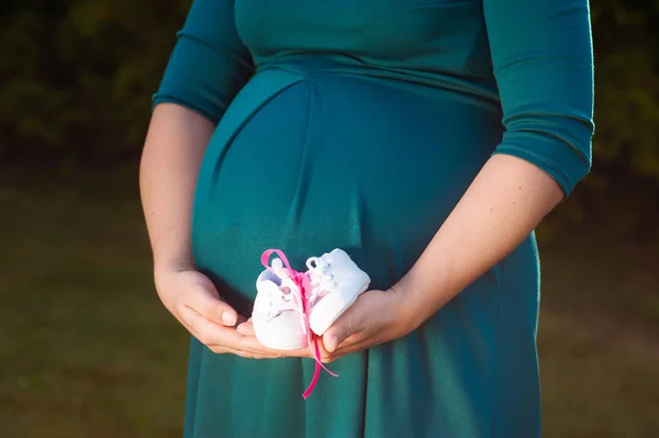 Kleine schoenen voor de ongeboren baby in de buik van een zwangere vrouw. Zwangere vrouw met kleine baby schoenen ontspannen thuis in de slaapkamer. Kleine schoenen voor de ongeboren baby in de buik van een zwangere vrouw — Stockfoto