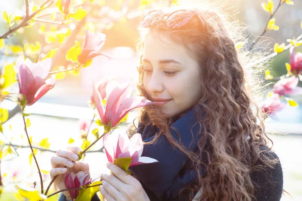 Young woman near blossoming magnolia flowers tree in spring park on sunny day. Beautiful happy girl enjoying smell in a flowering spring garden — Stock Photo, Image