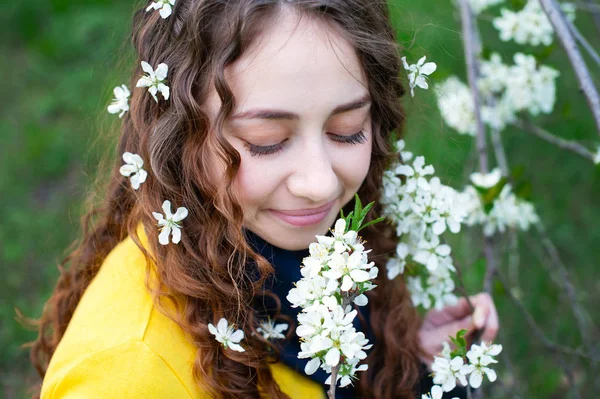 Счастливая молодая женщина наслаждается запахом цветов на фоне весеннего сада — стоковое фото