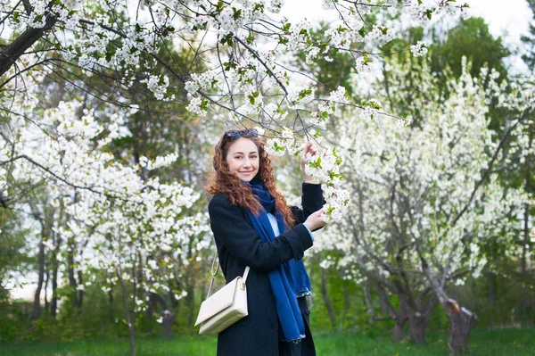 Portrait of a young beautiful fashionable woman in spring blossoming park. Happy girl posing in a blooming garden with white flowers — Stock Photo, Image