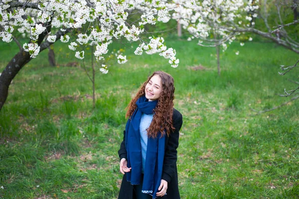 Portret młodej pięknej modnej kobiety w wiosennym parku kwitnących. Szczęśliwy dziewczyna stwarzające w kwitnący ogród z białymi kwiatami — Zdjęcie stockowe