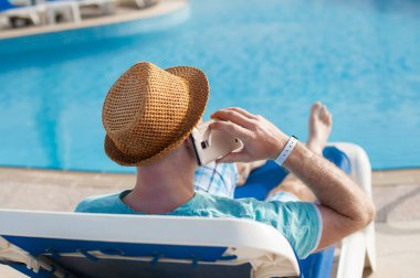 bir şezlong üzerinde yatan ve havuzun yakınında bir telefonda konuşan adam