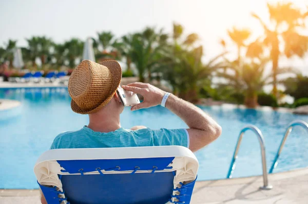 Hombre acostado en una tumbona y hablando por teléfono cerca de la piscina — Foto de Stock