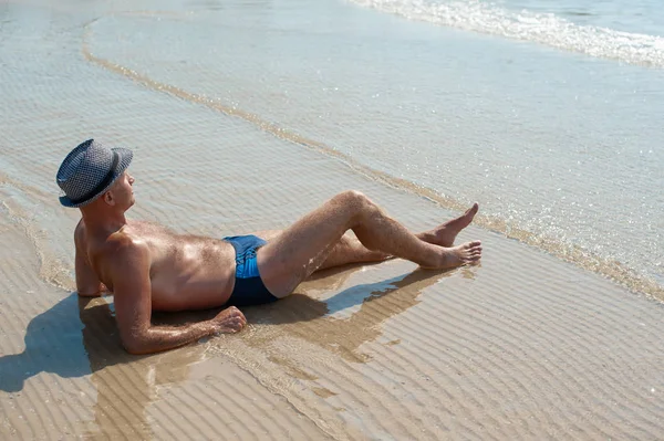 Snygg ung manlig modell man ligger på stranden sand klädd hipster sommar hatt njuter sommar semester nära havet — Stockfoto