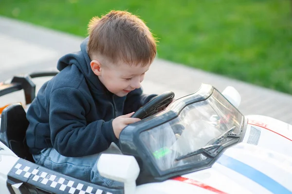 Schattige kleine jongen rijden mechanische speelgoed auto draaien van de stuurwiel met een blik van concentratie als hij speelt in een stadspark — Stockfoto