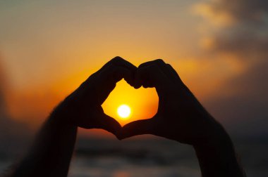 erkek ellerini gökyüzüne karşı kalp şeklinde güneş ışınları geçmek. Aşk kalp şeklinde elinde