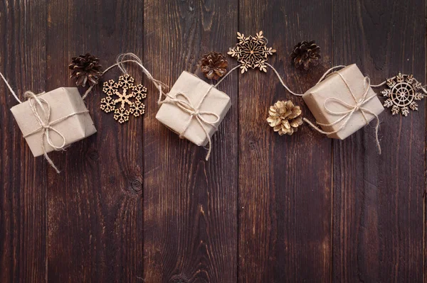 Tarjeta de felicitación navideña. Cajas de regalo Kraft con cuerda y copos de nieve, protuberancias sobre un fondo de madera con lugar para su texto —  Fotos de Stock