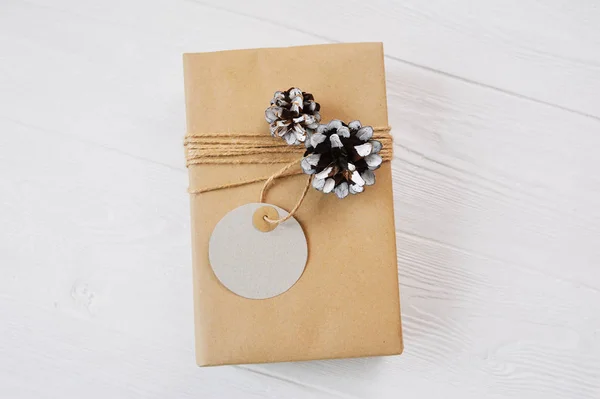 Κραφτ Χριστουγεννιάτικο κουτί δώρου με σχοινί, ταμπελάκι, κώνους σε λευκό φόντο. Κλείσιμο επάνω προβολή — Φωτογραφία Αρχείου
