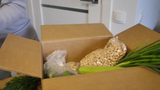 Voluntario en guantes con caja de donación de alimentos pone verduras para ayudar a los demás. caja de donación con productos alimenticios. Imágenes de vídeo Full HD — Vídeos de Stock