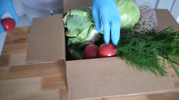 Voluntario en guantes azules sostiene verduras caja de donación de alimentos para ayudar a otros. paquete de donación con productos alimenticios. Imágenes de vídeo Full HD — Vídeos de Stock