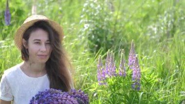 Bir buket lupinli güzel romantik kadın beyaz elbiseler içinde neşeyle gülümser ve mor lupin çiçekleriyle dolu bir tarlada oturur. Yumuşak seçici odak