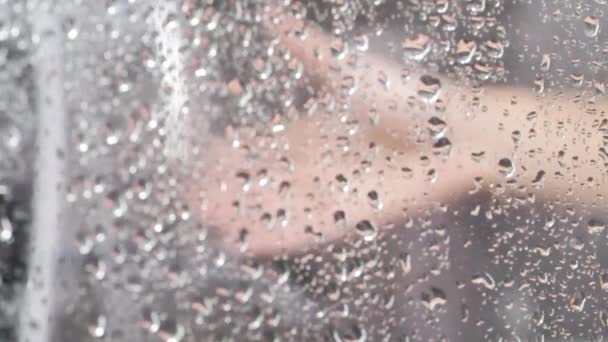Cerrar la textura de las gotas de agua en el vidrio y la mano de las mujeres. Grandes gotas de lluvia golpearon un vaso durante una ducha. 4K. Fondo de Bokeh — Vídeo de stock