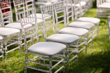 Beyaz yastıklı zarif şeffaf sandalyeler. Çimlere dizilmiş. Düğün konukları için şık koltuklar yaratıyor.